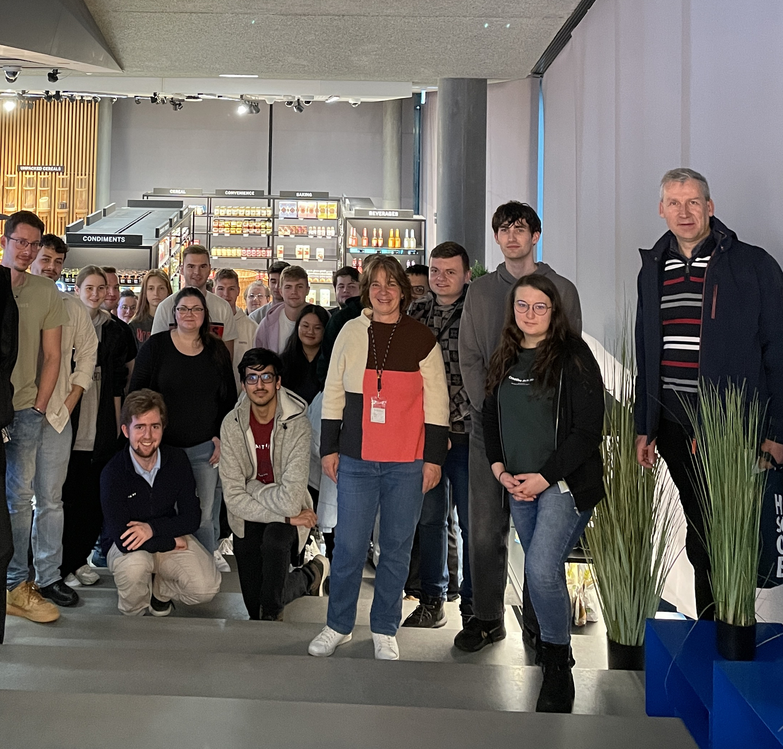 Gruppe von Studierenden steht auf einer Treppe und im Hintergrund sieht man einen Showroom von SAP