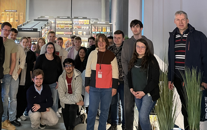 Gruppe von Studierenden steht auf einer Treppe und im Hintergrund sieht man einen Showroom von SAP