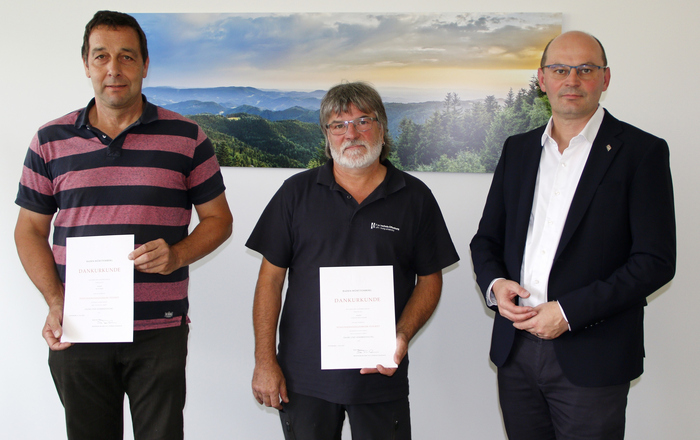 Rudi Kirn (links) und Stefan Hollinger (Mitte) stehen im Büro des Rektors Stephan Trahasch (rechts) vor einem Bild mit einer Schwarzwaldlandschaft.