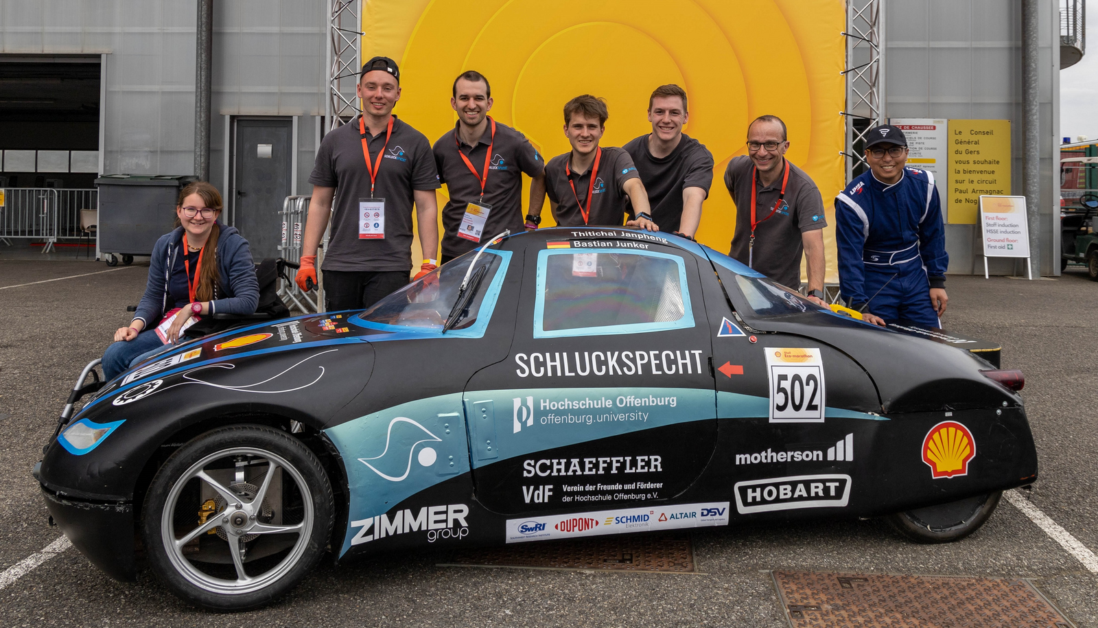 Die sieben Teammitglieder stehen hinter dem Fahrzeug, eine legen eine Hand auf die Karosserie 