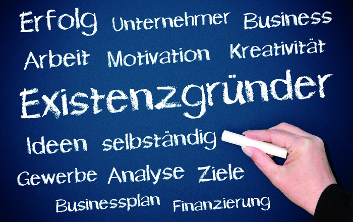Eine Hand schreibt mit Kreise verschiedene passende Begriffe rund um das Wort Existenzgründer auf eine Tafel. 
