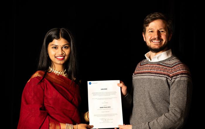 A woman in traditional Indian dress and a man in a woolen sweater hold a certificate