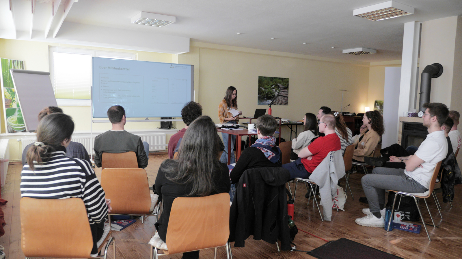 Eine Frau steht vor einer Gruppe sitzender junger Menschen und spricht zu diesen