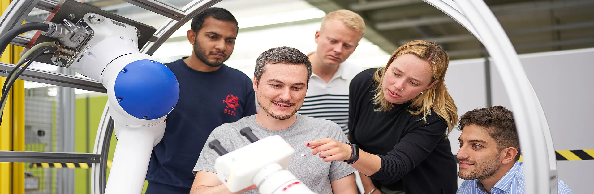Fünf Studierende im Labor um einen Roboterarm