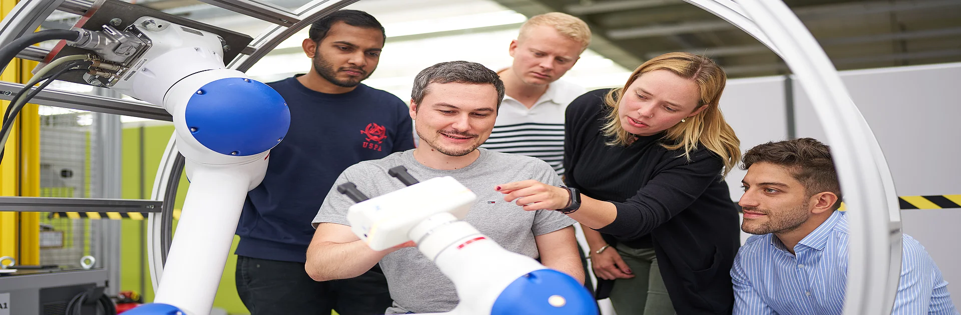 Fünf Studierende im Labor um einen Roboterarm