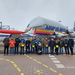 Die Projektbeteiligten stehen auf dem Firmengelände vor einem Airbus