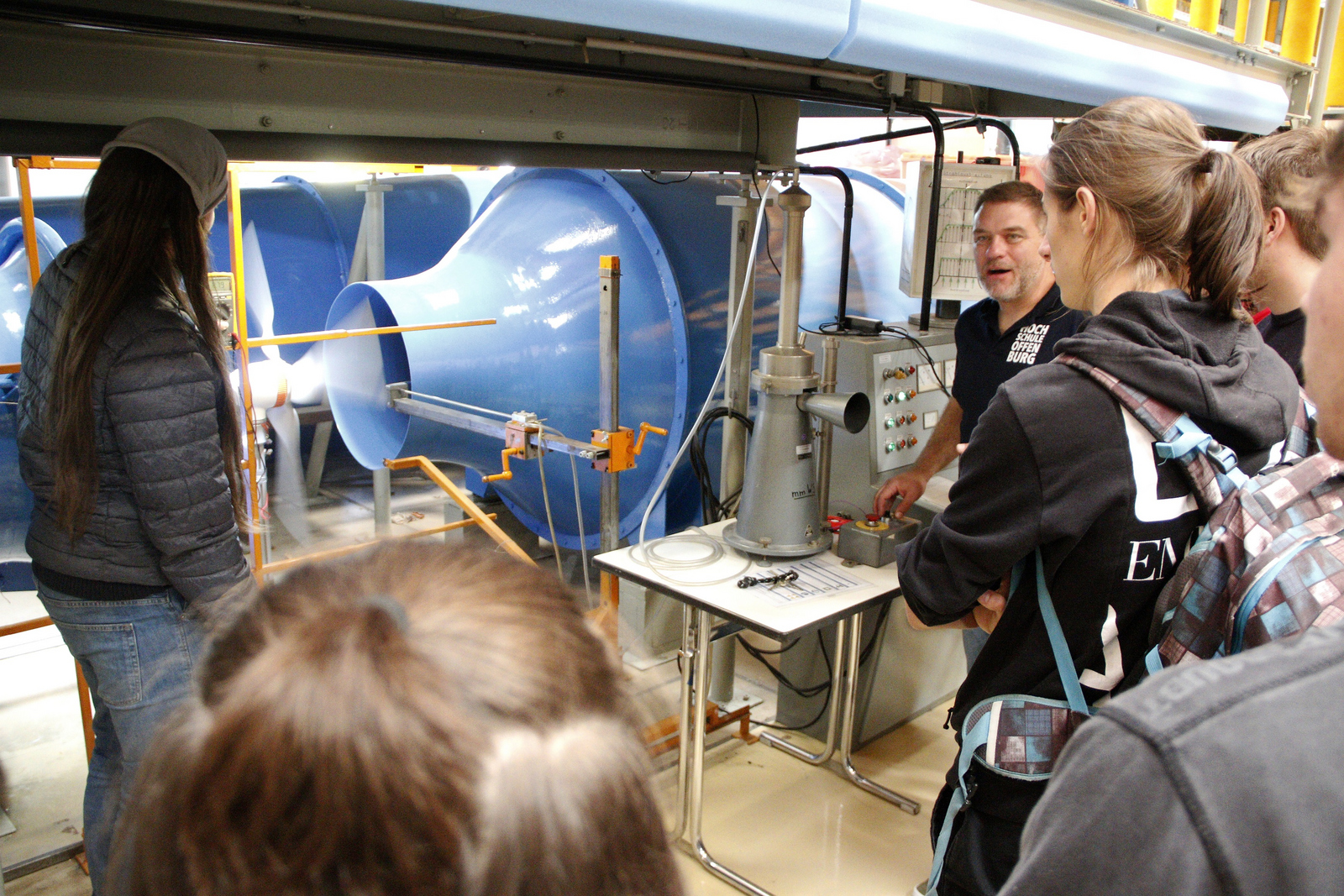 Jörg Ettrich und einige Schüler im Strömungskanal, wo ein Windrad im Luftstrom rotiert und ein Schüler ein Messgerät hält