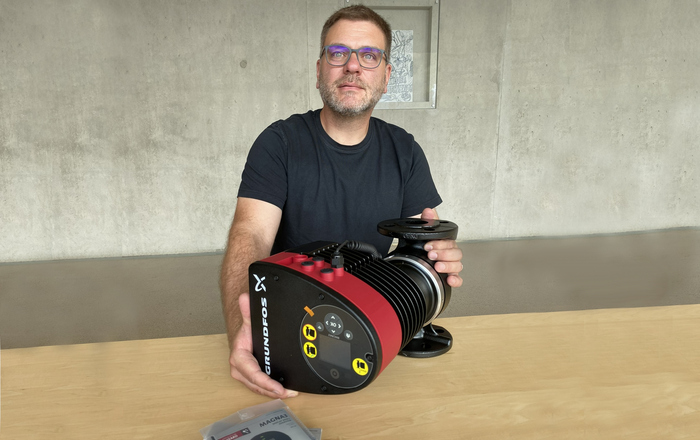 Jörg Ettrich präsentiert die Pumpe die vor ihm auf einem Holztisch liegt 