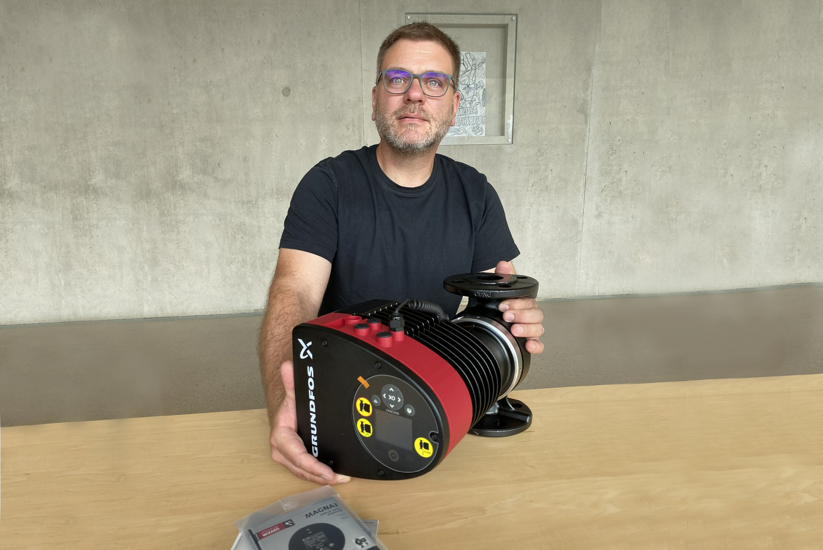 Jörg Ettrich präsentiert die Pumpe die vor ihm auf einem Holztisch liegt 