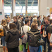 Blick vom großen Saal ins Foyer mit vielen Messeständen die umringt sind von Studierenden