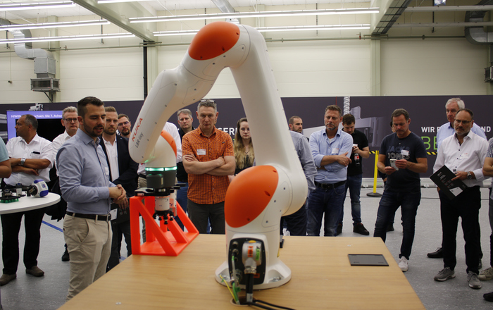 Zahlreichen Menschen stehen um einer Roboterarm herum