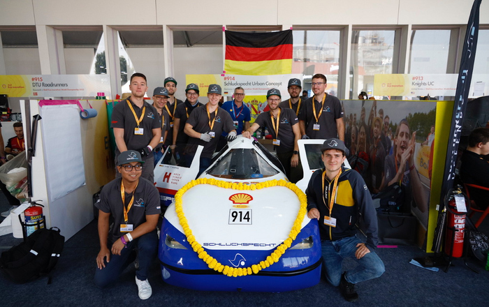 Team steht um das mit einem gelben Blumenkranz geschmückte Auto herum