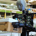 Ein humanoider Roboter steht vor einer Maschine und hält ein Paket vor einen Bildschirm.  