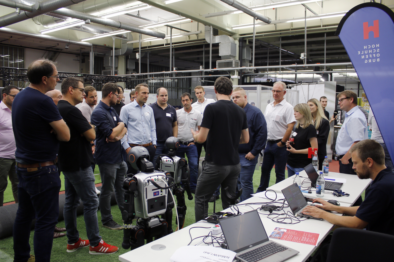 2025-07-15 wvib Robotik Tag Ganz viele Menschen stehen um zwei humanoide Roboter herum, ein Mann erklärt etwas