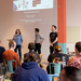4 Studierende stehen vor einer Gruppe sitzender Studierender und präsentieren mit Hilfe einer Präsentation auf einer Leinwand hinter ihnen ihr Projekt
