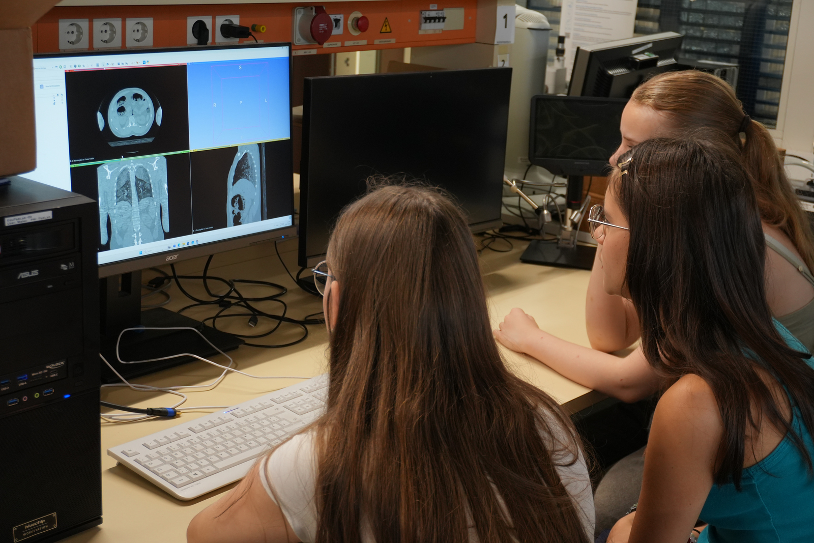 2025-07-18 PM Besuch Klosterschulen Körperscans Drei Mädchen sitzen vor einem Computer auf dem Schichtaufnahmen von einem Schädel und einem Oberkörper zu sehen sind