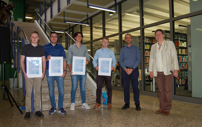 Die Preisträger, Firmenvertreter Alexander Becker und Prof.in Elke Mackensen (von links) stehen im Foyer von Gebäude B vor einer Treppe