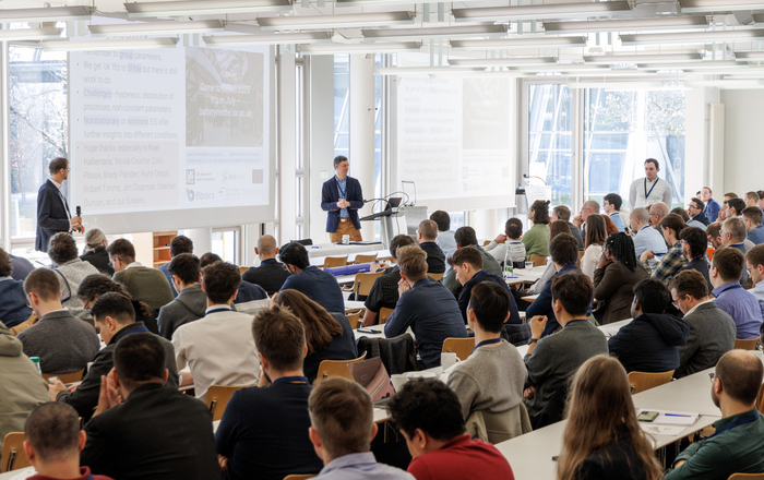 Zwei Männer stehen vor zahlreichen sitzenden Konferenzteilnehmenden