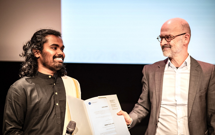 Zwei Männer schauen sich an und halten eine Urkunde zwischen sich