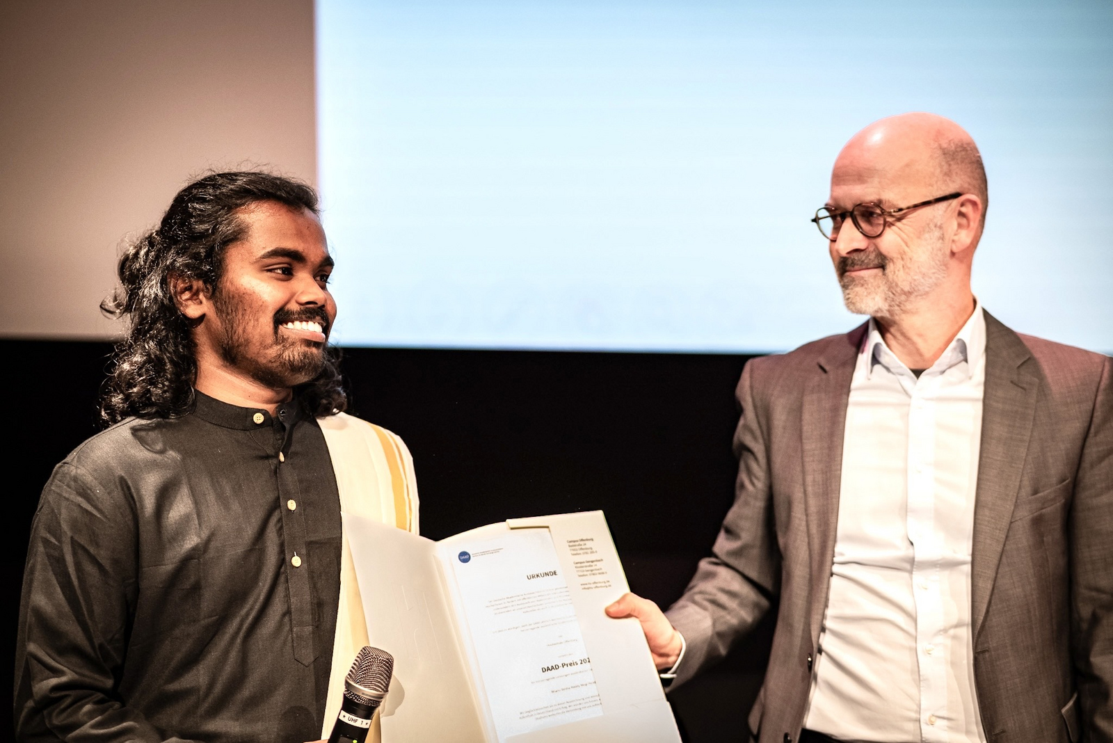 Zwei Männer schauen sich an und halten eine Urkunde zwischen sich