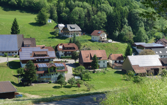 Häuser mit und ohne Photovoltaik-Anlage auf dem Dach an einem sonnenbeschienenen Schwarzwaldhang.