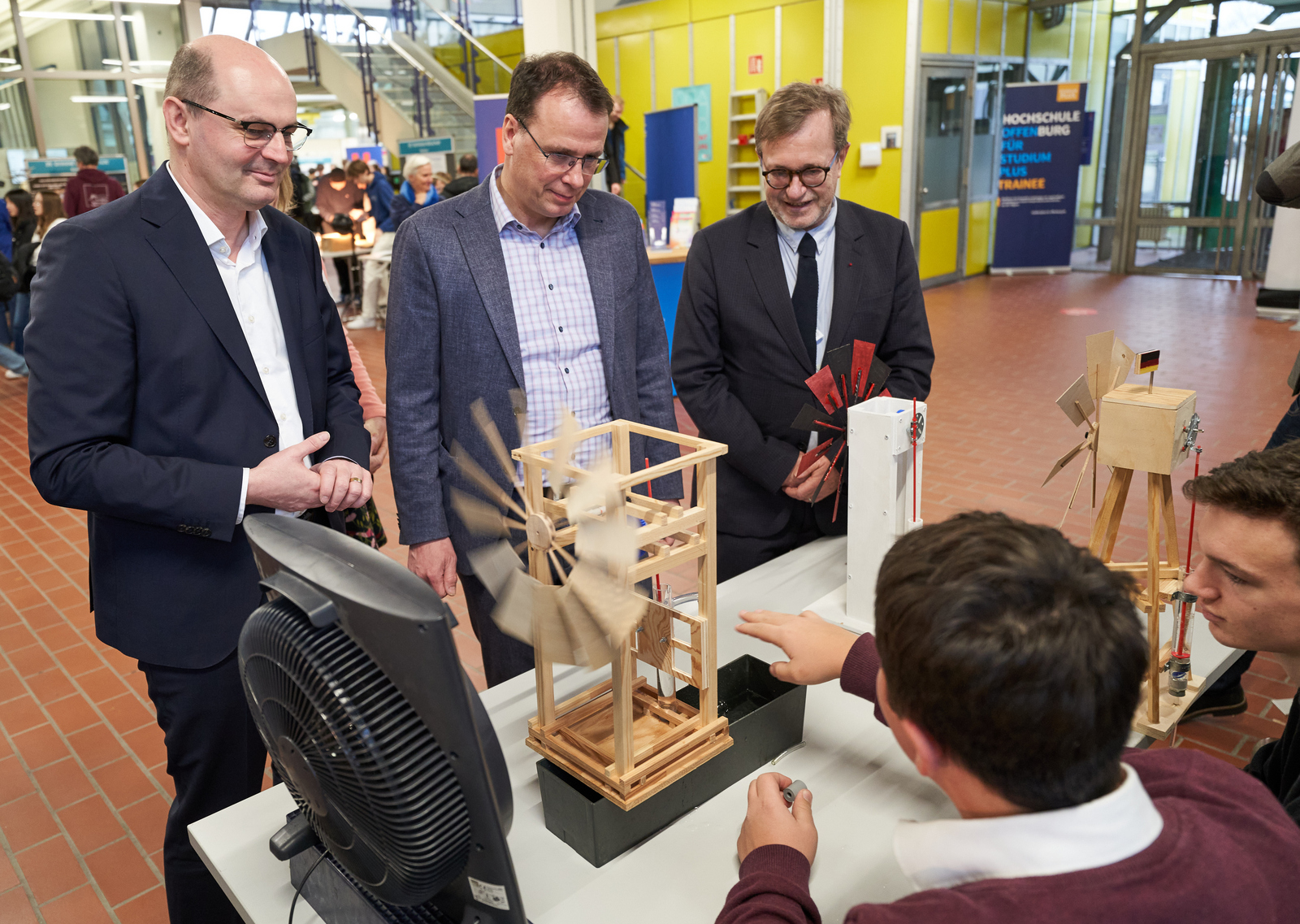 Trahasch, Faron, Schebesta lassen sich an einem Stand von Schülern die Windradpumpe erklären