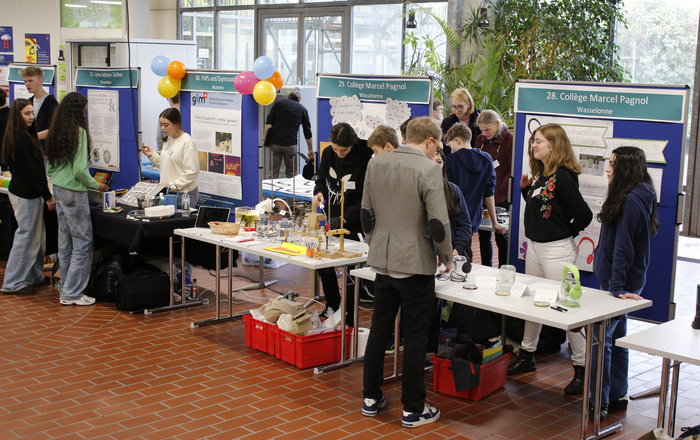 Schüler an präsentieren an Tischen mit Stellwänden dahinter ihre Forschungsarbeiten