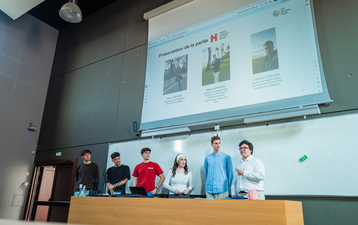 Sechs junge Leute stehen an einem langen Rednerpult vor einer Leinwand und stellen sich vor