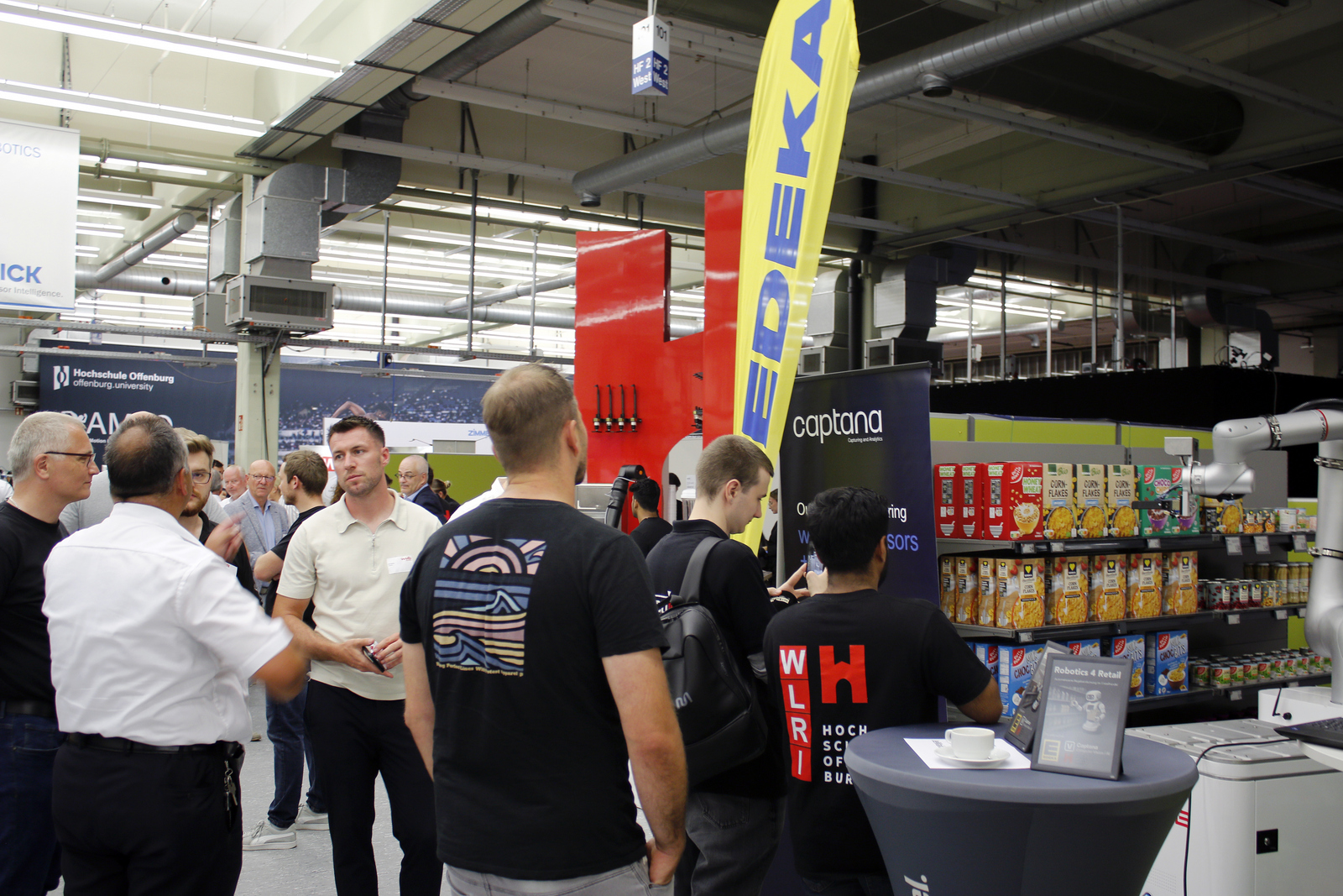 2025-07-15 wvib Robotik Tag Mehrere menschen beobachten wie ein Roboter etwas in einem Supermarktregal greift
