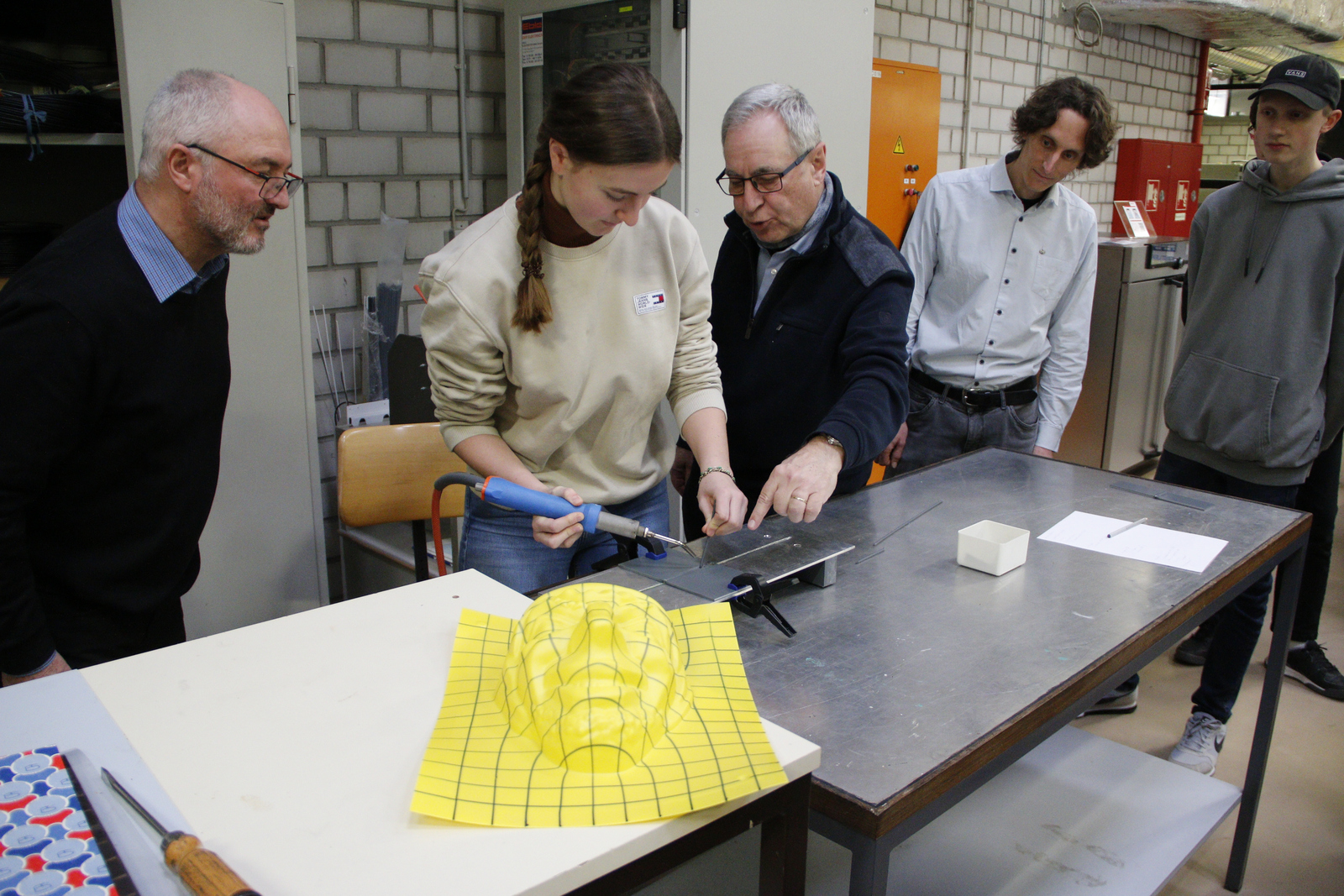 Eine Schülerin versucht sich unter Anleitung der Professoren sowie den Blicken ihres Lehrers und eines Mitschülers beim Thermoschweißen.
