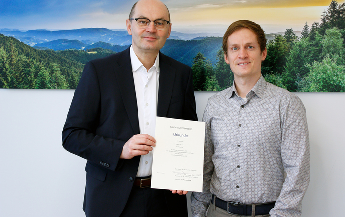 Zwei Männer stehen vor einem Schwarzwaldfoto und halten ein Urkunde 