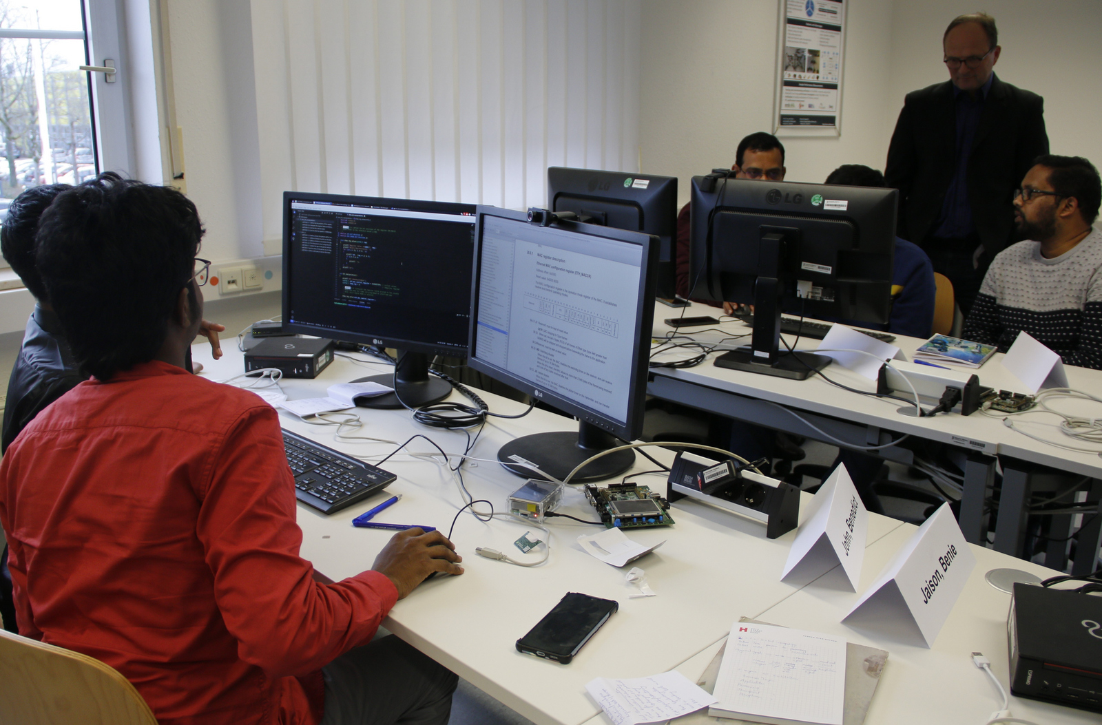 Teilnehmende sitzen an Computern und programmieren im Hintergrund beobachtet Prof. Sikora ihr Arbeit