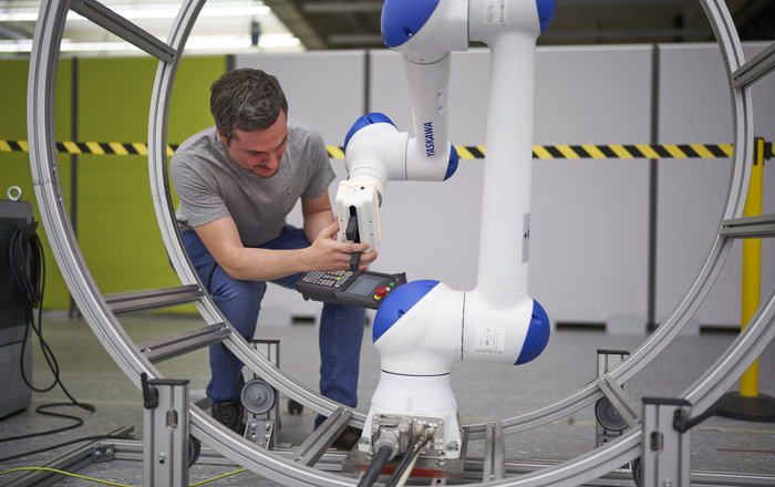 Ein Mann mit einer Elektroniksteuerung in der Hand arbeitet an einem Industrieroboter