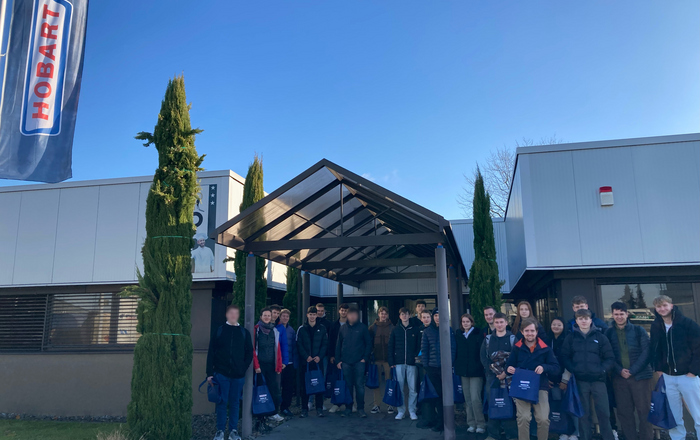 startING Studierende stehen als Gruppe vor dem Haupteingang von Hobart bei blauem Himmel. Links weht eine Hobartfahne im Wind.