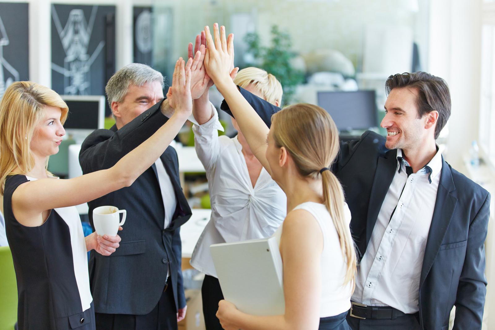 Fünf schick gekleidete Personen stehen im Kreis und geben sich ein High-Five.