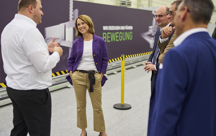 Doktorand Nikolai Hangst mit Landeswissenschaftsministerin Petra Olschowski und Rektor Prof. Dr. Stephan Trahasch im Gespräch an der 22,5 Meter lange Roboterachse im Work-Life Robotics Institut.