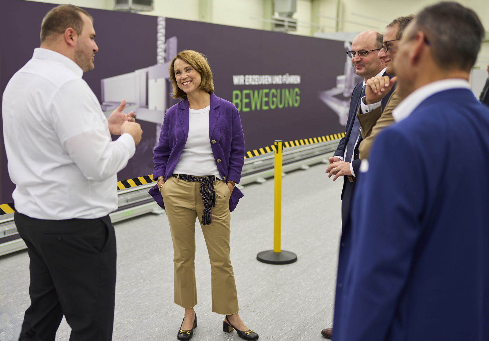 Doktorand Nikolai Hangst mit Landeswissenschaftsministerin Petra Olschowski und Rektor Prof. Dr. Stephan Trahasch im Gespräch an der 22,5 Meter lange Roboterachse im Work-Life Robotics Institut.