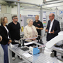 Eine Gruppe von Menschen steht um einen Tisch mit einerm Roboterarm herum, ein Mann erklärt etwas 
