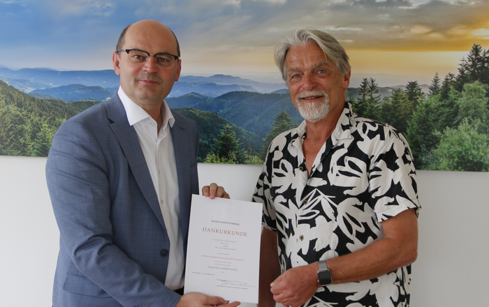 Stephan Trahasch (links) überreicht Markus Moser (rechts) vor einem Schwarzwaldpanorama stehend die Urkunde