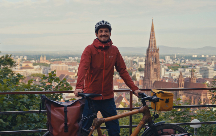 Ein Mann steht neben seinem Fahrrad auf einem kleine Berg hinter ihm im tiefergelegenen Tal ist das Freiburger Münster zu sehen