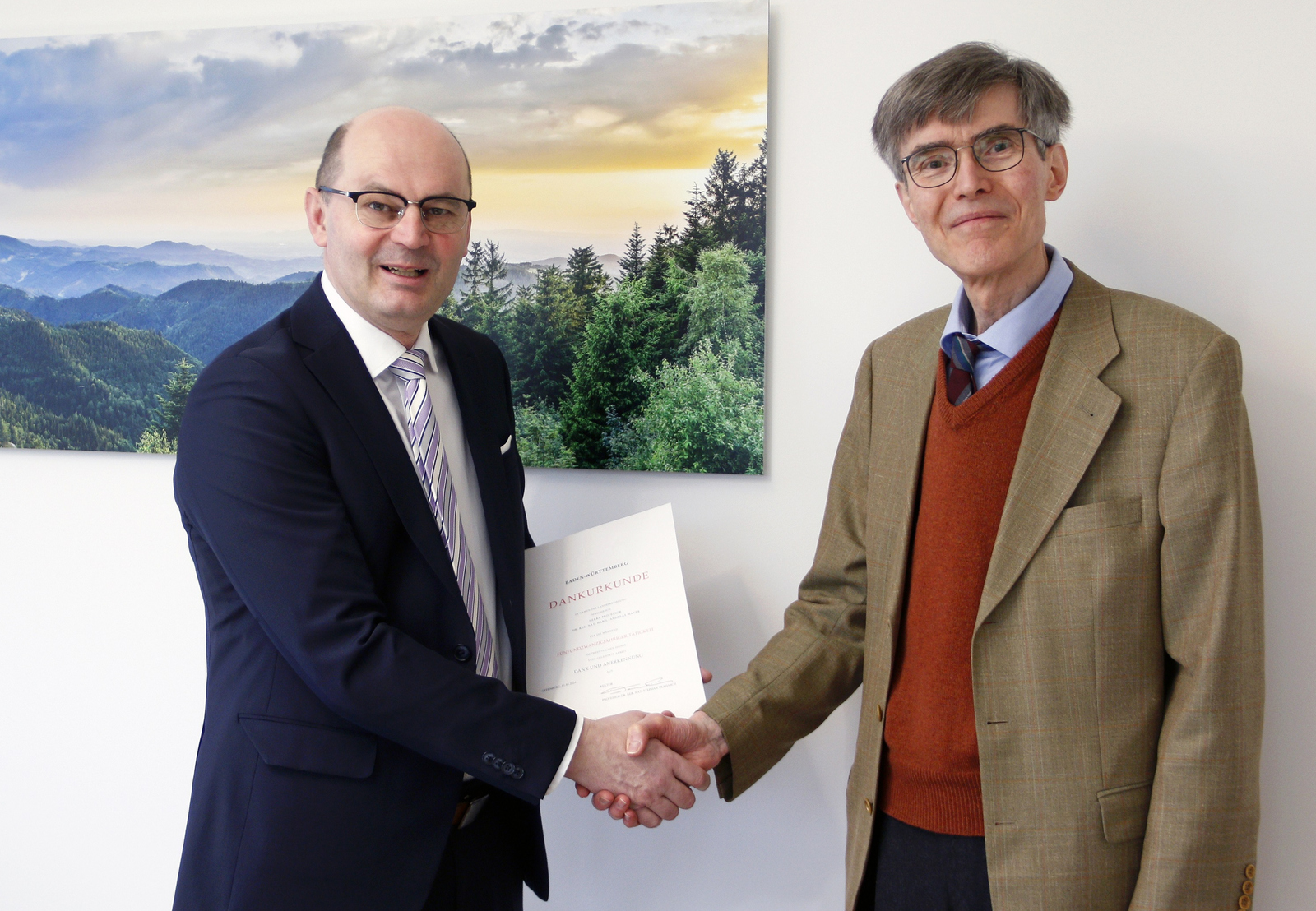 Rektor Stephan Trahasch steht vor einem Schwarzwald-Bild, schüttelt Andreas Mayer die HAnd und überreicht die Urkunde  