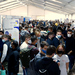 Ausstellende und Studierende mit Maske im Messezelt.