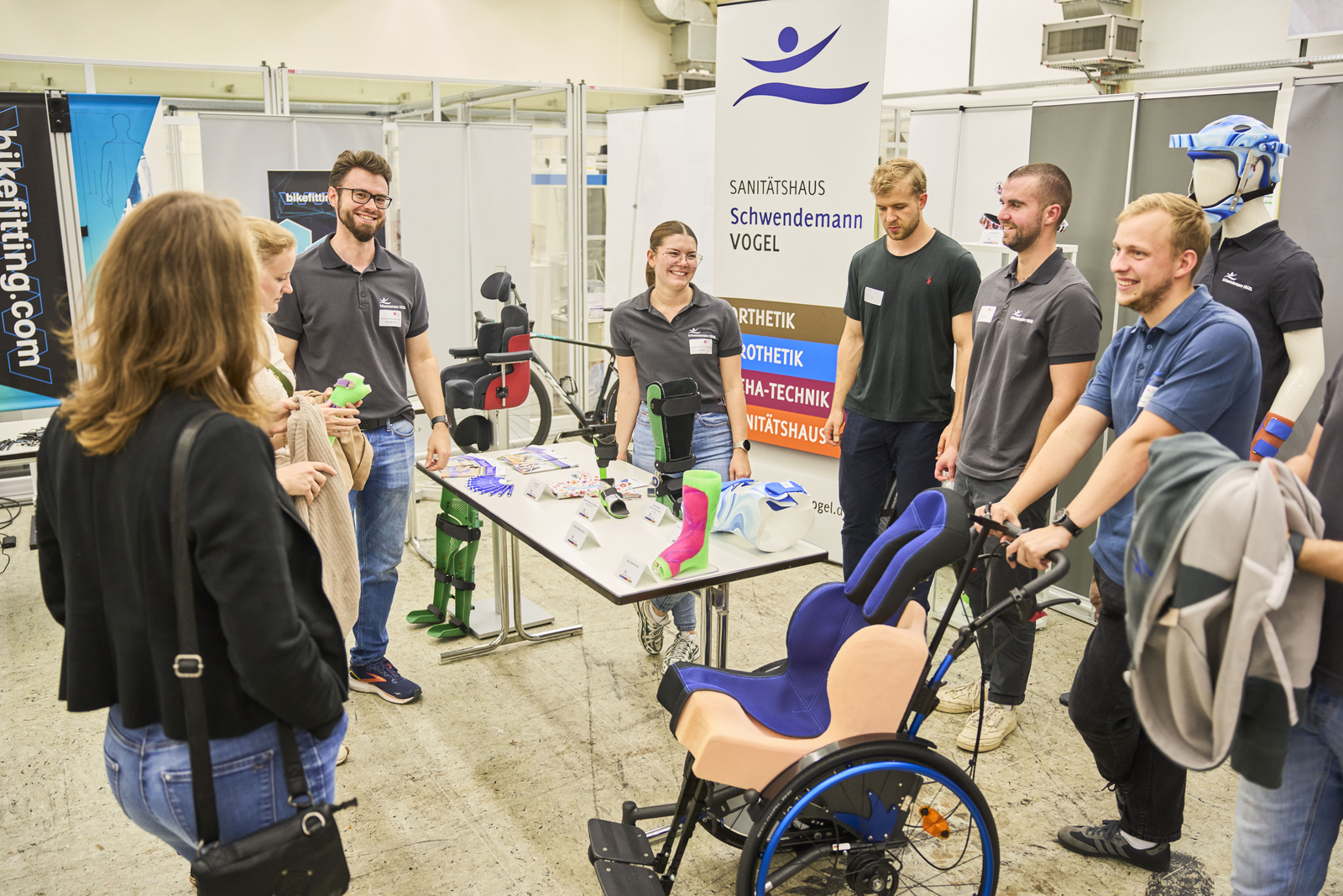 Menschen stehen um einen Stand mit Rollstühlen, Orthesen, etc. herum