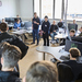 Zwei Studenten stehen umringt von sitzenden und stehenden Schülerinnen und Schülern in einem Computerraum und erzählen etwas