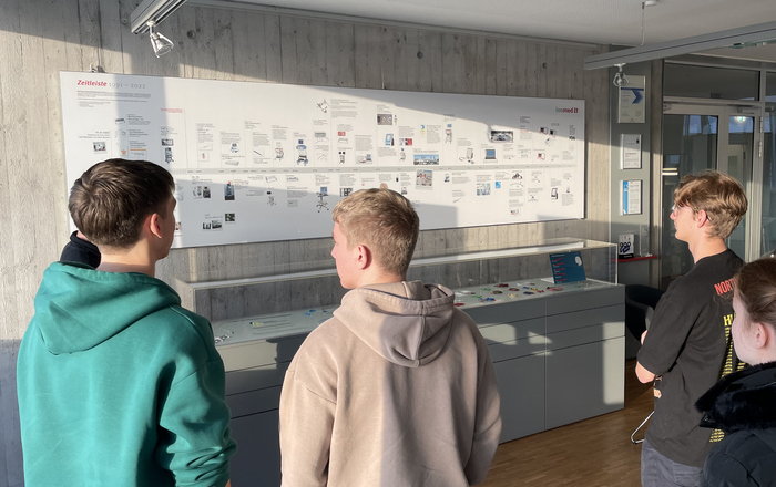 Gruppe von Studierenden steht vor Infotafel und Schaukasten bei inomed