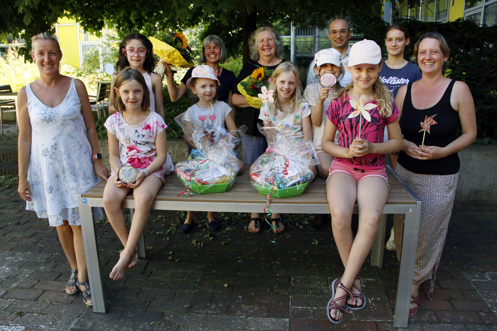 Gruppenbild die Kinder sitzen mit den geschenken draußen auf einem Tisch, die Erwachsenen stehen neben und hinter dem Tischv