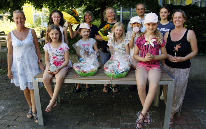 Gruppenbild die Kinder sitzen mit den geschenken draußen auf einem Tisch, die Erwachsenen stehen neben und hinter dem Tischv