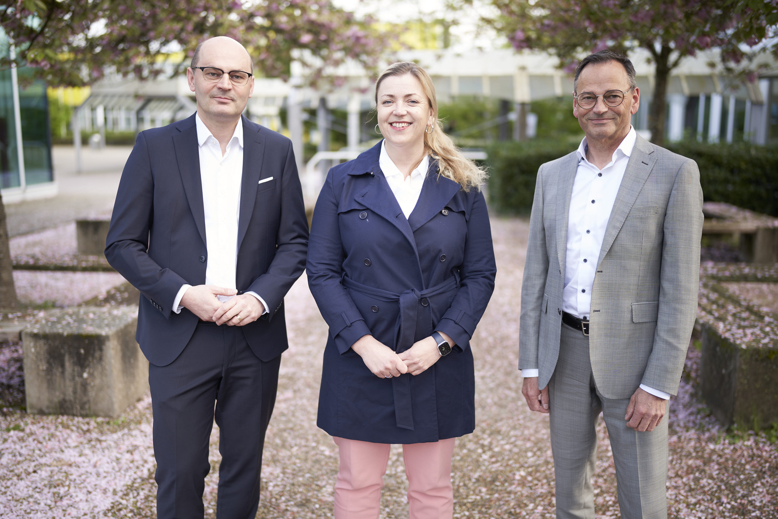 Stephan Trahasch, Ulrike Kahle-Roth und Klaus Erdrich (von links) stehen unter blühenden Bäumen auf dem Campus. 