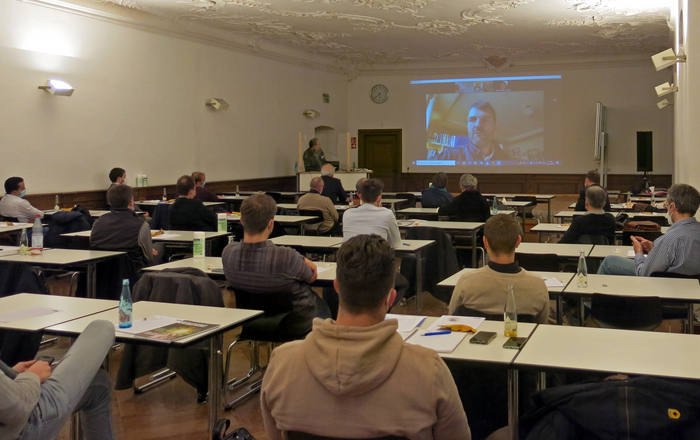 Im Barocksaal des Klosters Gengenbach sitzenden die Zuhörenden vor einer leinwand auf der Live-Übertragung des Vortrags von Dr. Mario Herger aus dem Silicon Valley zu sehen ist. 