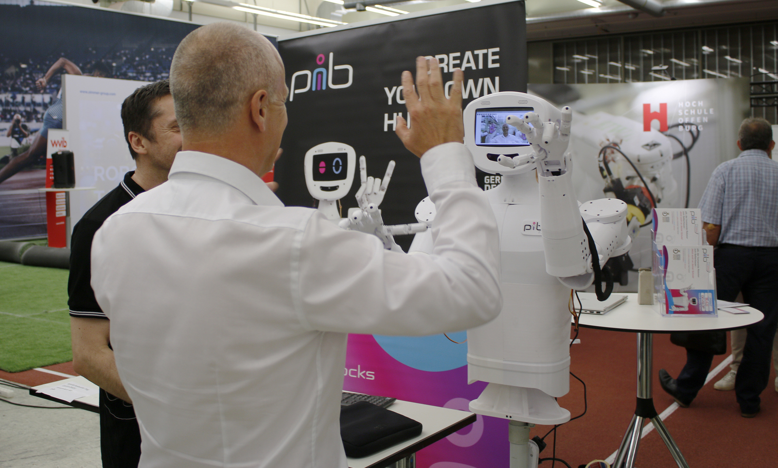 2025-07-15 wvib Robotik Tag Ein Mann hebt die Hände und ein humanoider Roboter mit einem Kamerabild im Kopf macht es ihm nach